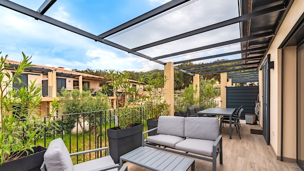 Une terrasse extérieure couverte, aménagée avec des meubles gris, une table et des plantes en pot.