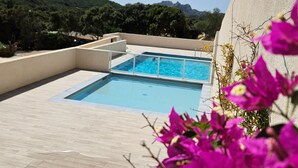 Une piscine sur le toit, avec une eau d’un bleu cristallin, entourée d’une terrasse en bois et offrant une vue sur des collines verdoyantes.
