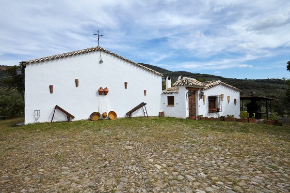 A white building with a cross on the roof, a small annex, and a cobblestone ground.