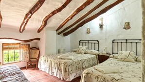 Een kamer met twee bedden, een stoel, een raam en een rustiek plafond.