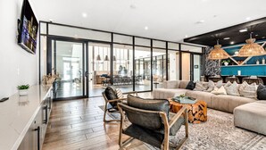 A modern living room with a sofa, chairs, and a coffee table. There is a kitchen area visible through a glass door. - Sunny 2-Bed Oasis: Pool & Gym in Apollo Beach (Apollo Beach)