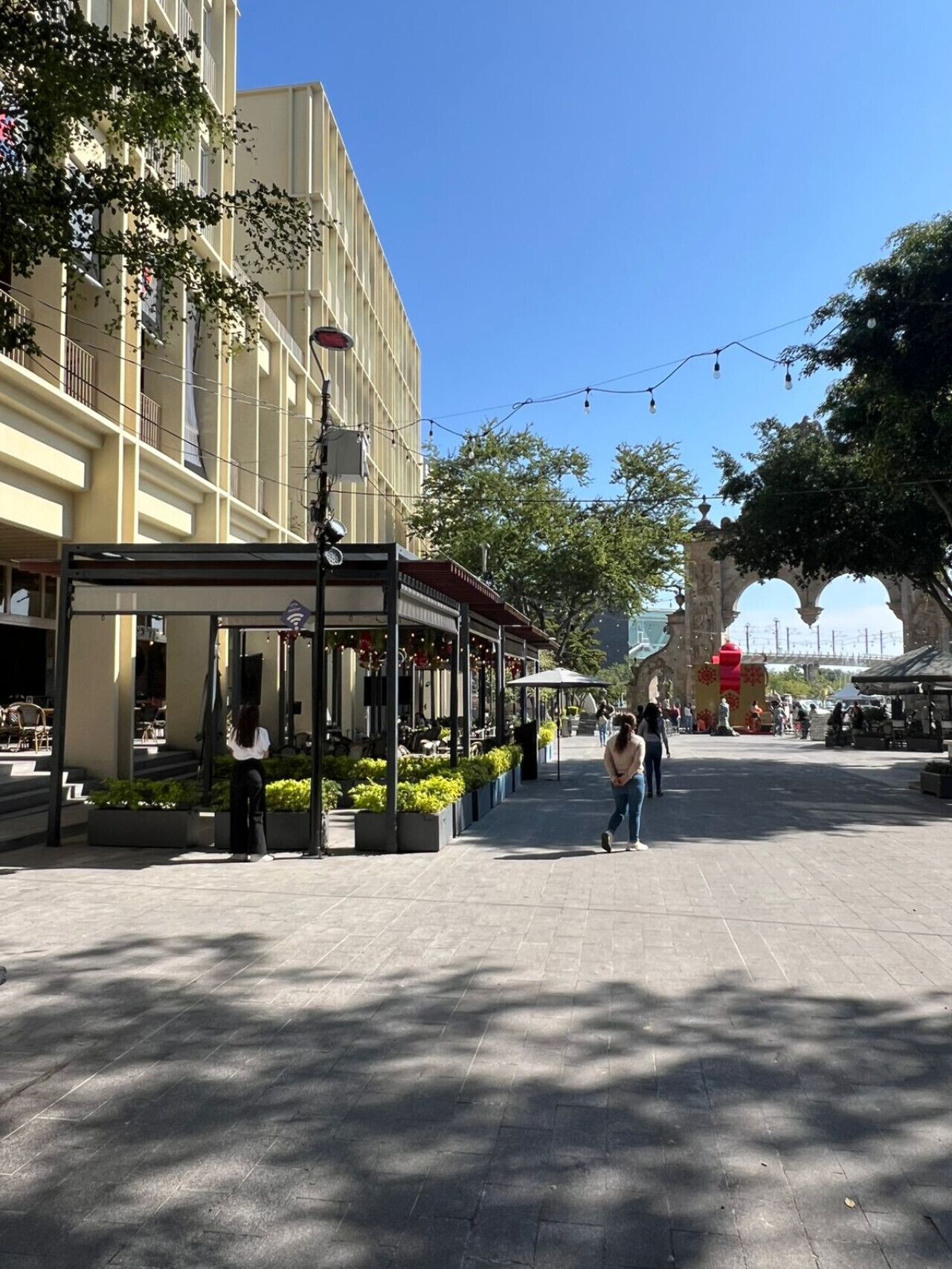 Uma praça externa com café, áreas de estar e um arco de pedra.