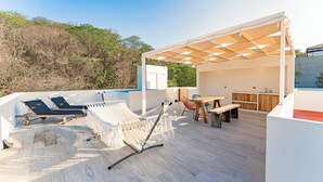 Una terrazza sul tetto con un'amaca, poltrone relax, un tavolo e una zona ombreggiata.