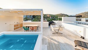 Area piscina sul tetto con tavolo e sedie, un barbecue e una zona salotto coperta.