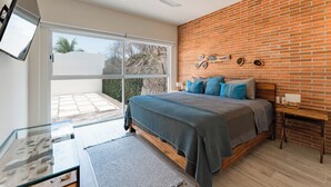 Camera da letto con un letto grande, un tavolino in vetro, un muro in mattoni e una porta scorrevole in vetro che dà su un balcone.