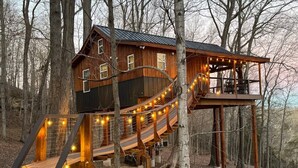 Une cabane en bois dotée d’une terrasse et d’un escalier, entourée d’arbres.
