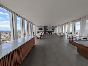 Eine geräumige, moderne Hotelhalle mit einer langen Rezeption, mehreren Sitzbereichen und großen Fenstern mit Blick auf die Stadt.