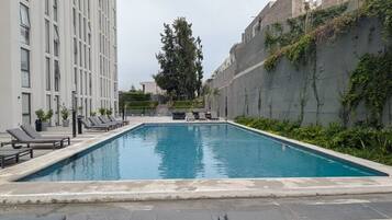 Ein rechteckiger Swimmingpool mit Liegestühlen und einem Baum im Hintergrund.