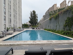 Ein rechteckiger Swimmingpool mit Liegestühlen und einem Baum im Hintergrund.