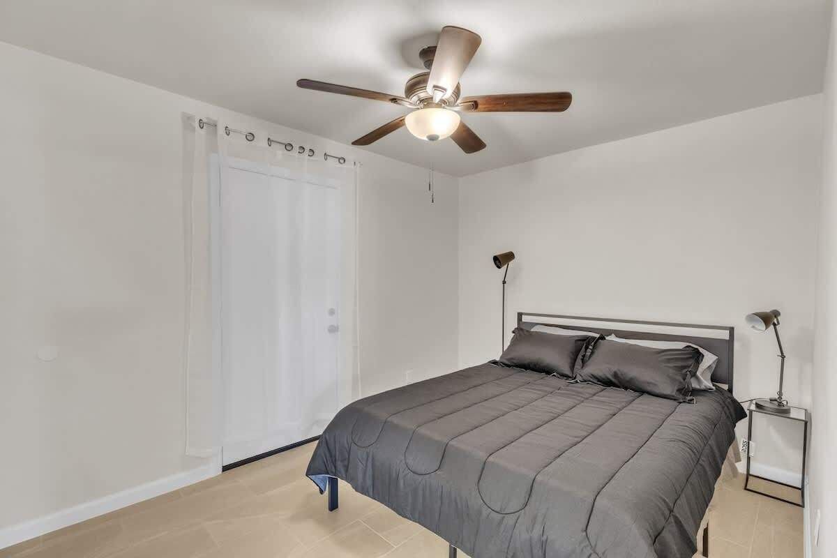 Ein Schlafzimmer mit einem Bett, einem Deckenventilator, einem Nachttisch mit Lampe und einer weißen Tür.