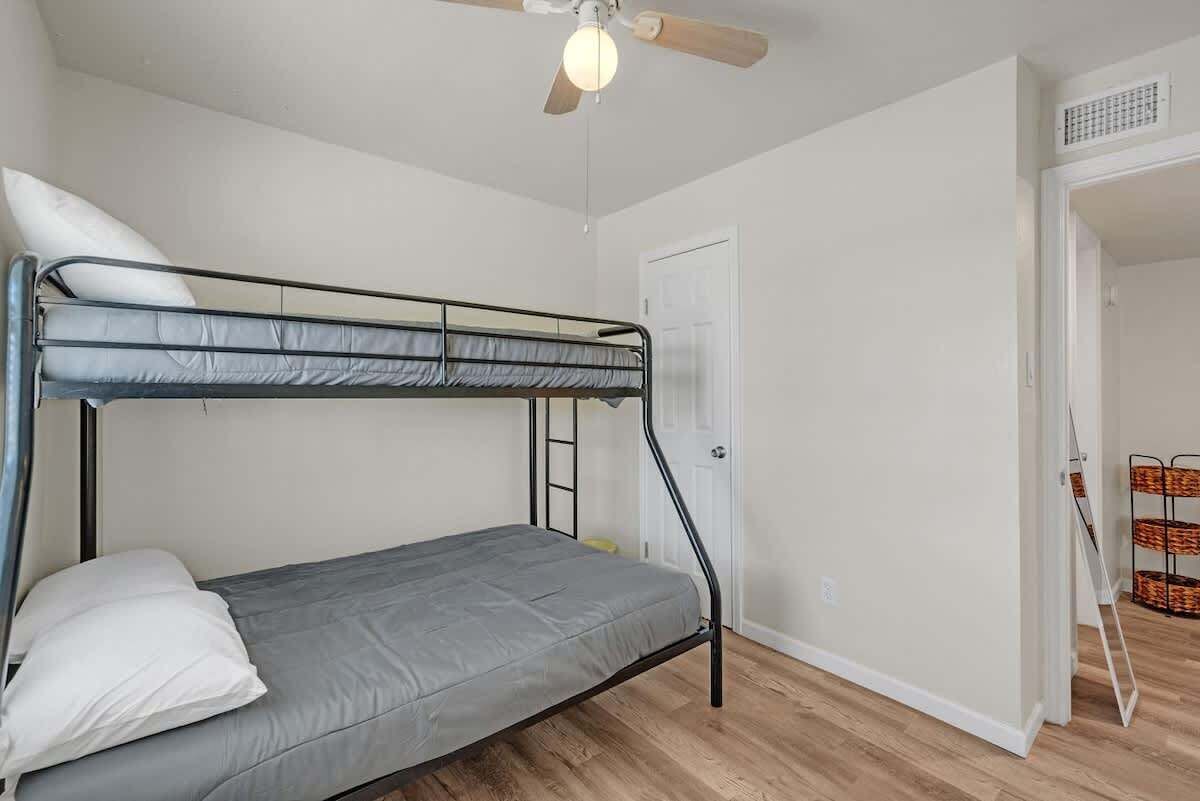Une chambre individuelle avec un lit superposé, un ventilateur de plafond, une porte et une petite table avec des paniers.