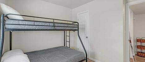 Une chambre individuelle avec un lit superposé, un ventilateur de plafond, une porte et une petite table avec des paniers.