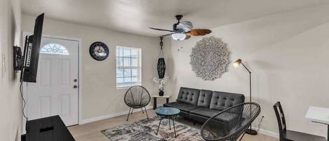 Un salon comprenant un canapé, des fauteuils, une table basse, un téléviseur et un ventilateur de plafond.