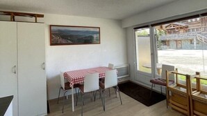 A dining area with a table and chairs, a painting on the wall, and a view of a building outside. - 350m from ski slopes, Ground floor, terrace, tv, 24m², Alpe d'Huez (L'Alpe d'Huez)