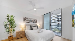 A modern bedroom with a bed, bedside table, lamp, and a large window with a view of a building. - KozyGuru | Rockdale | Cozy Apt near Train Station (Rockdale)