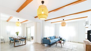 Un salón amplio con un sofá azul, una mesa de comedor con sillas y dos lámparas de mimbre colgantes.