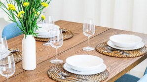 Mesa de comedor dispuesta con platos blancos, cubiertos y copas de vino, rodeada de sillas azules.