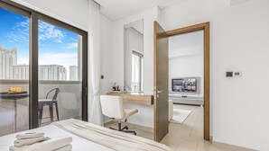 A hotel room with a bed, a desk, a chair, a TV, and a balcony with a city view. - New 2BR with Pool & Gym in Green Sobha Community (Dubai)