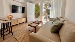 Sala de estar moderna com sofá, mesa de centro, TV e varanda com vista para áreas verdes.
