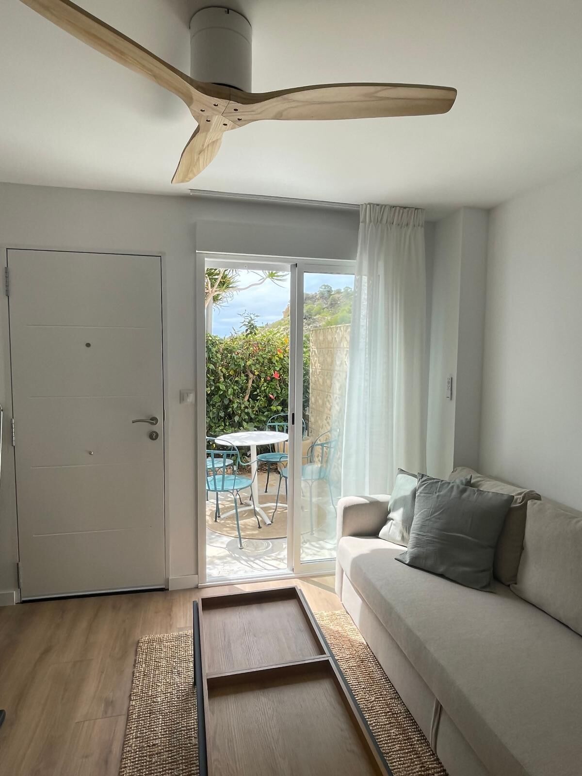 A modern living room with a sliding glass door leading to an outdoor patio, a ceiling fan, a sofa, and a small table.