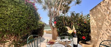 An outdoor dining area with a table set for two, surrounded by greenery and a decorative wall.