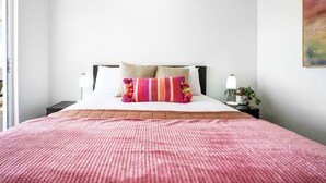 A neatly made bed with a pink blanket, a colorful striped pillow, and two bedside lamps.