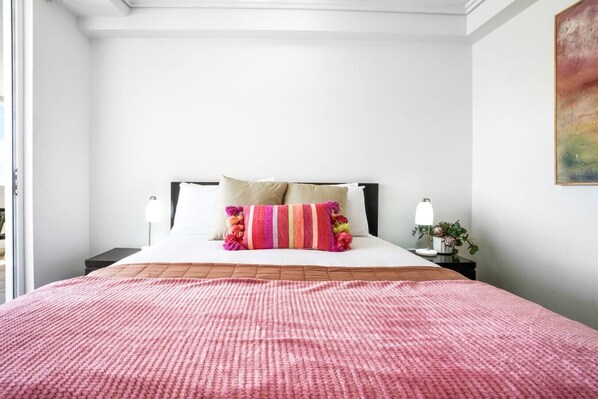 Uma cama bem arrumada com um cobertor rosa, um travesseiro listrado e duas luminárias de cabeceira.