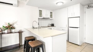 A modern kitchen with white cabinetry, a central island with stools, a built-in oven, and a refrigerator.