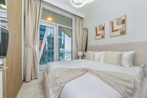 A modern hotel room with a large bed, a view of the city, and two abstract wall art pieces.