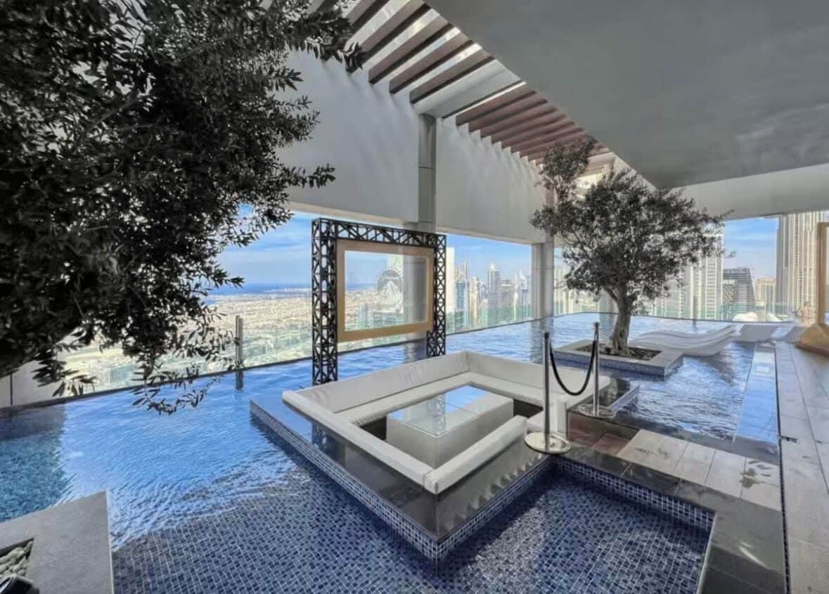 Una piscina infinita interior de lujo con vistas a la ciudad, rodeada de arquitectura moderna y plantas de interior.