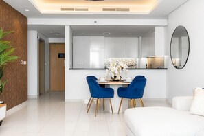 A modern kitchen with white cabinets, a central island, and a dining area with blue chairs.