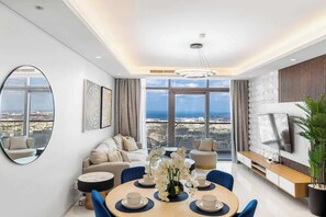 A modern living room with a dining area, large windows with a city view, a round table with chairs, and a sofa set. - Ultra Luxurious! Stunning Views, 64th Floor Pool (Business Bay)