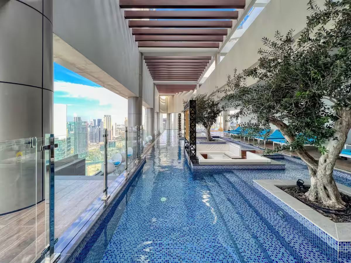 Ein moderner, überdachter Pool mit blauen Mosaikfliesen, einer Glastrennwand und Blick auf die Stadtlandschaft.