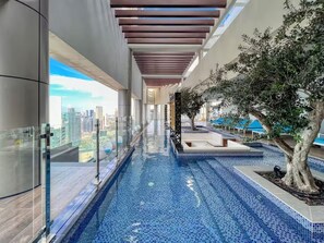 A modern indoor pool with blue mosaic tiles, a glass railing, and a view of the cityscape.