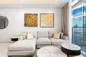 Una sala moderna con un sofá seccional, una mesa de centro redonda y dos cuadros abstractos en la pared.