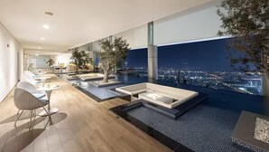 A modern hotel lobby with a pool area, seating, and a city view at night. - Ultra Luxurious! Stunning Views, 64th Floor Pool (Business Bay)