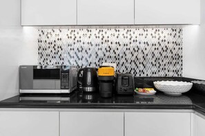 A modern kitchen with a microwave, coffee maker, toaster, and a bowl on the counter. - Ultra Luxurious! Stunning Views, 64th Floor Pool (Business Bay)