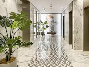 A hallway with a geometric patterned floor, glass walls, and a potted plant.