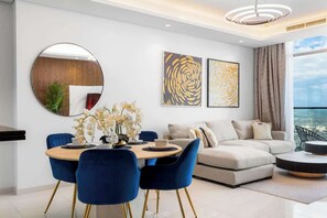 A modern living room with a round dining table, blue chairs, a sofa, and artwork on the wall. - Ultra Luxurious! Stunning Views, 64th Floor Pool (Business Bay)