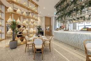 A modern interior with a dining area featuring a long table and chairs, surrounded by shelves with decorative vases and potted plants.