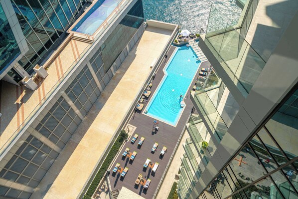 A rooftop pool with lounge chairs and a glass balustrade, surrounded by modern buildings.