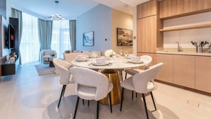 A modern dining area with a round table, white chairs, and a gold base. There is a kitchen area with wooden cabinets and a sink. - Luxury 2BR  with Stunning Lake View in Business Bay (Dubai)