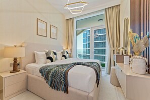 A modern hotel room with a large bed, a bedside table with a lamp, a dresser, and a view of a cityscape through the window.