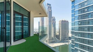 A modern balcony with glass doors, a green artificial turf area, and a view of high-rise buildings. - Luxury 2BR  with Stunning Lake View in Business Bay (Dubai)