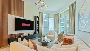 A modern living room with a flat-screen TV displaying "NETFLIX," a comfortable sofa set, a coffee table, and a large window offering a city view. - Luxury 2BR  with Stunning Lake View in Business Bay (Dubai)