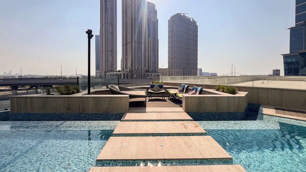 Une piscine sur le toit, avec des chaises longues et une vue dégagée sur les grands immeubles qui se dressent à l’arrière-plan.