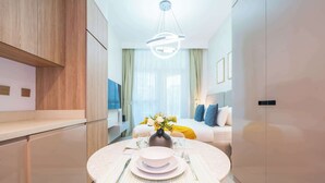 A modern hotel room with a dining area, a bed with a yellow blanket, and a vase with flowers. - Stylish Studio in Business Bay (Dubai)