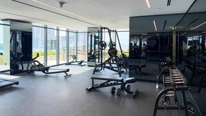 A modern gym with various exercise equipment, large windows, and a view of the city. - Stylish Studio in Business Bay (Dubai)