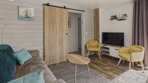 A modern living room with a sofa, two chairs, a TV, and a wooden door. - Chalet for 6 - Heated Pool - Terrace (Bretignolles-sur-Mer)