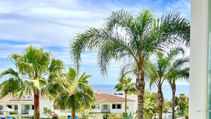 A pool area with palm trees, a thatched-roof structure, and a view of the sea. - Rancho Mirafoles apartment, Sea Views (Mijas)